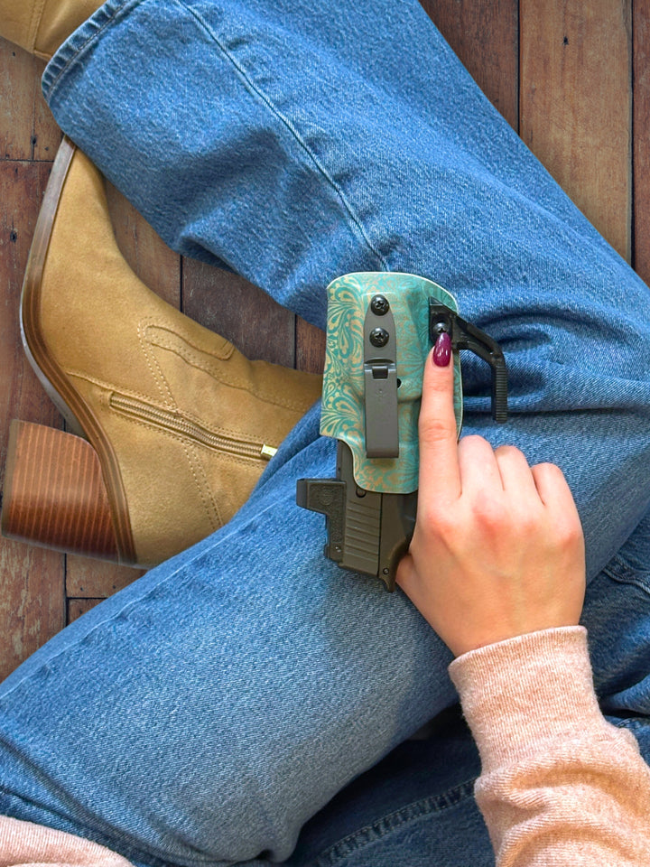 Betty 2.0 IWB holster in Boutique Patina with concealment wing, resting on a knee in jeans next to suede boots #color_boutique-patina