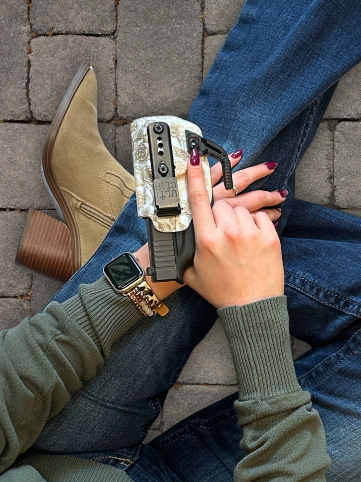 Hand holding the Betty 2.0 IWB holster in Tea-Stained Roses with Ulticlip and concealment wing, styled with jeans and suede boots #color_tea-stained-roses
