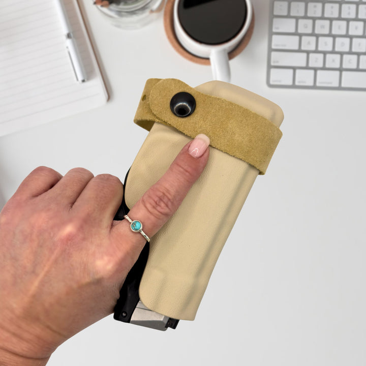 Hand holding a beige holster, office setting in the background.