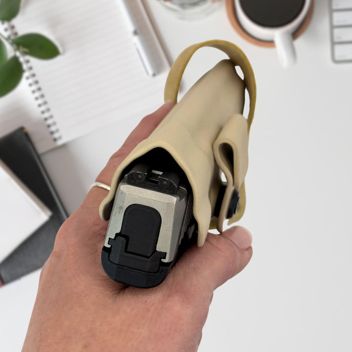 Hand holding a beige holster and black firearm with a blurred office background