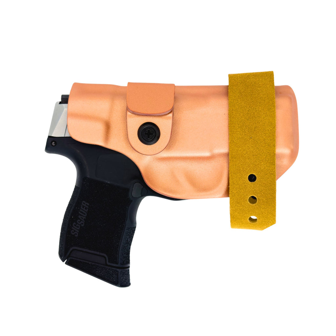 Pistol in a rose gold metallic holster with a tan strap on a white background